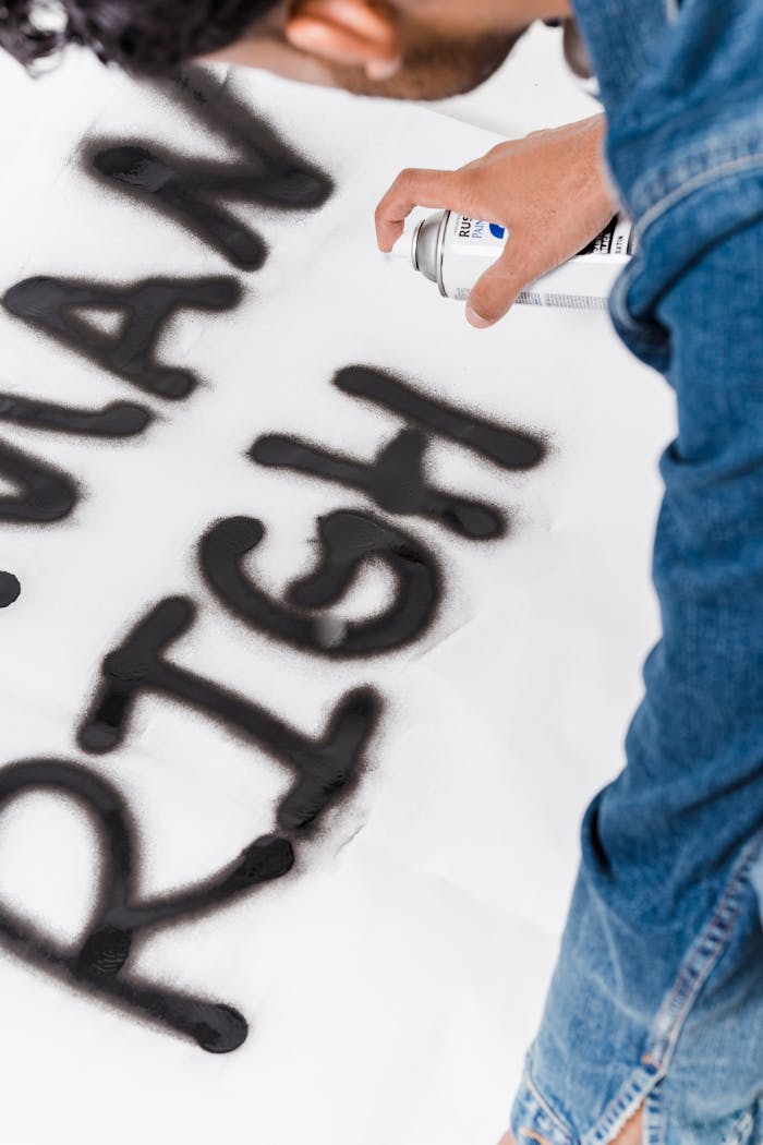 Adult spraying graffiti art on canvas promoting human rights awareness.