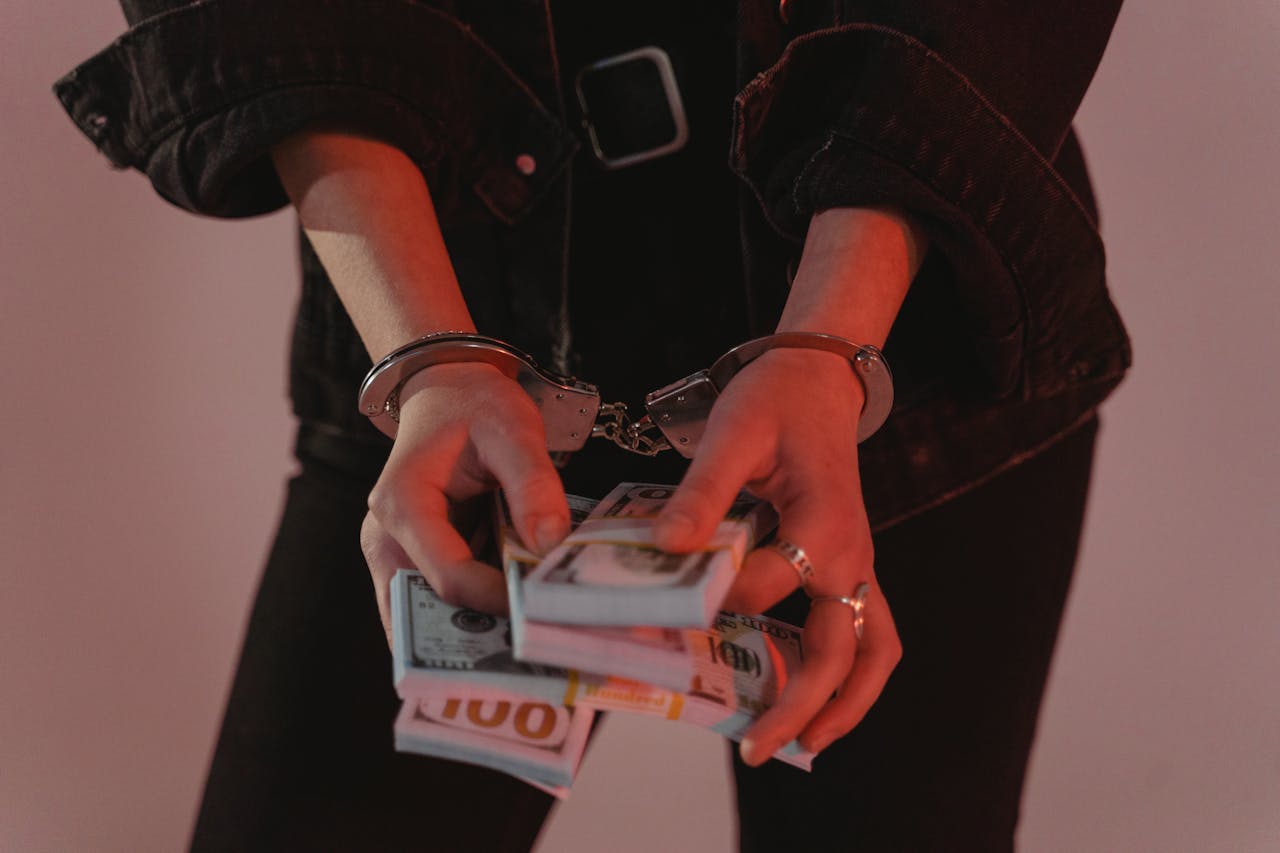 about-us Close-up of hands holding cash with handcuffs, symbolizing crime and punishment.